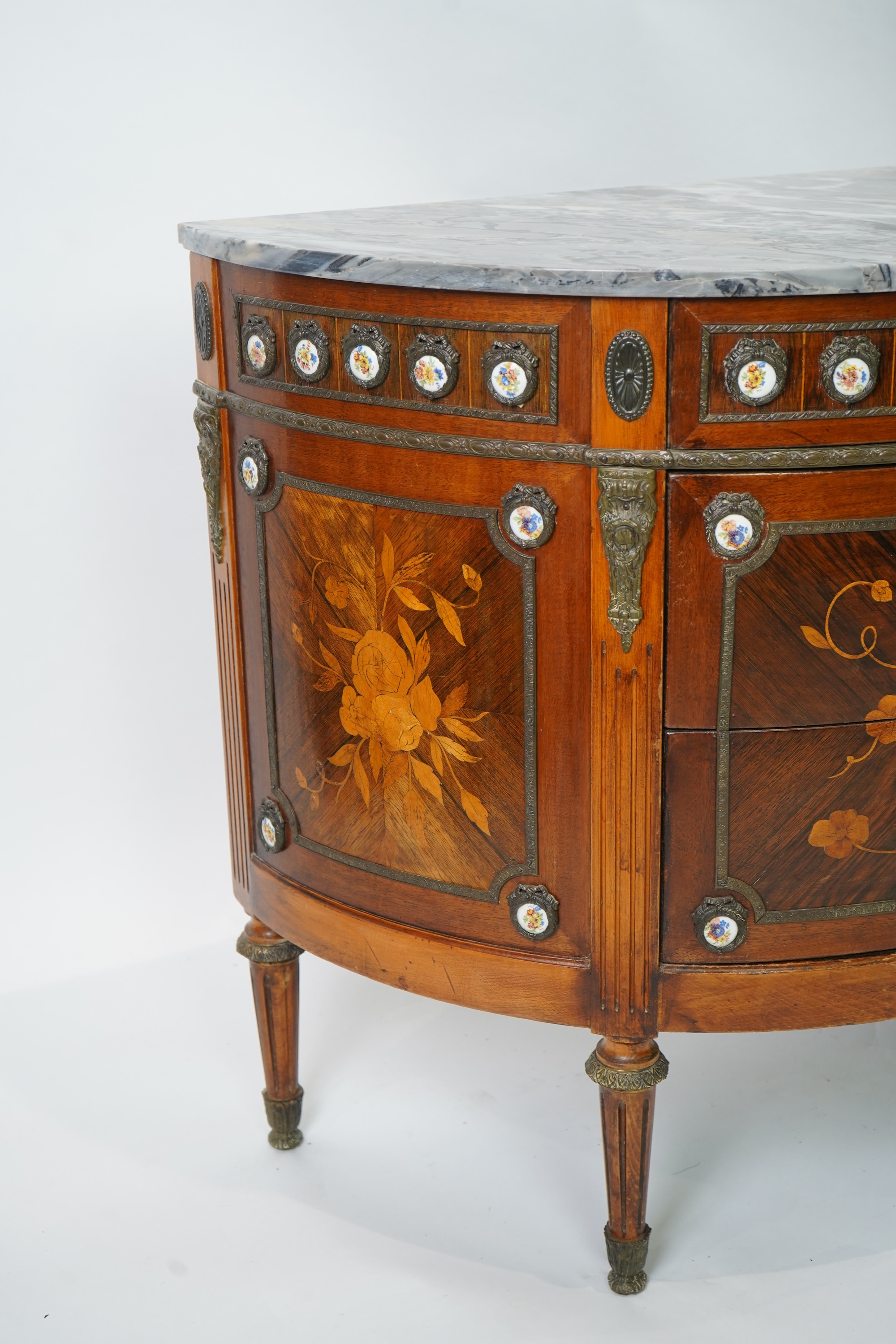 A pair of early 20th century French marquetry inlaid, gilt metal and porcelain mounted rosewood and beech demi-lune commodes